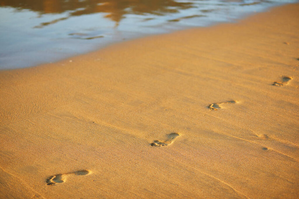 Stopy při západu slunce se zlatým pískem. pláž, vlna a kroky při západu slunce - Fotografie, Obrázek