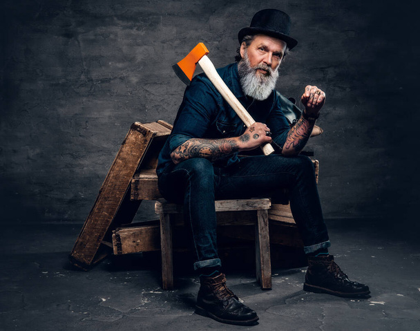 Senior man woodcutter with axe sitting on wood - Фото, изображение