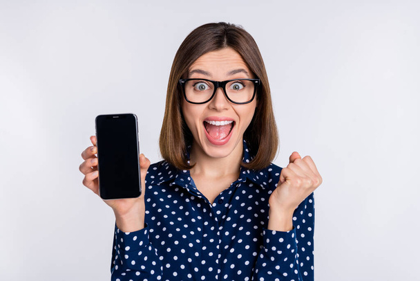 Photo of crazy lady hold phone show touchscreen empty space rejoice sale wear dotted blouse isolated grey color background - 写真・画像