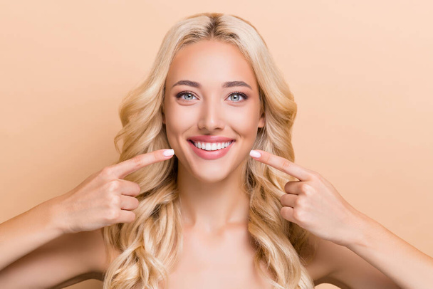 Retrato de atractiva chica de pelo ondulado alegre demostrando dientes sanos perfectos aislados sobre fondo de color pastel beige - Foto, Imagen