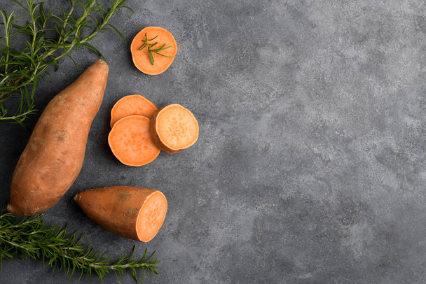 Raw whole orange sweet potato and slices of batatas with fresh rosemary on grey concrete background, top view, copy space, flat lay - Foto, imagen