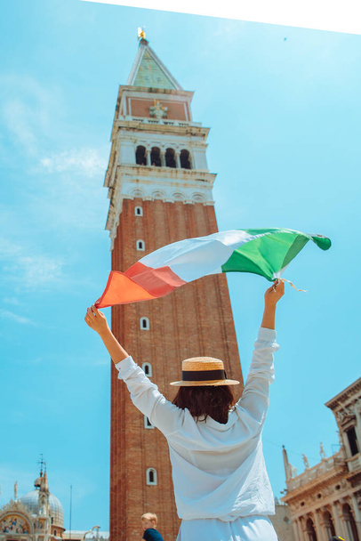женщина с итальянским флагом в центре венецкой квадратной колокольни на заднем плане летнее время Кампаниле ди Сан-Марко - Фото, изображение