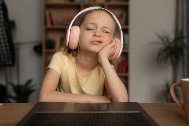 Bored Little Girl Using Laptop Wearing Earphones At Home - Фото, изображение