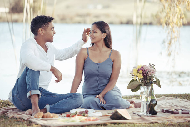 Eres tan hermosa. Foto completa de una joven pareja sentada junto a un lago en una cita y disfrutando de un picnic. - Foto, imagen