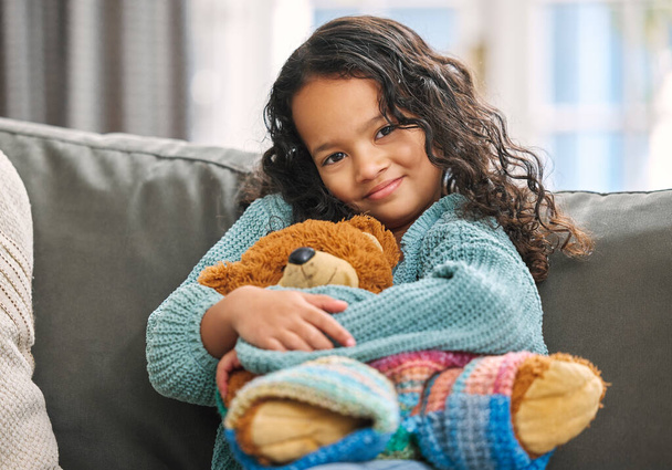 Komfort in einem Spielzeug. Aufnahme eines entzückenden kleinen Mädchens, das allein zu Hause auf dem Sofa sitzt und einen Teddybär in der Hand hält. - Foto, Bild