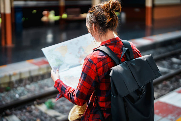 nyár, pihenés, nyaralás, utazás, portré egy aranyos ázsiai lány nézi a térképen, hogy tervezzen egy utat, miközben vár a vasútállomáson. - Fotó, kép