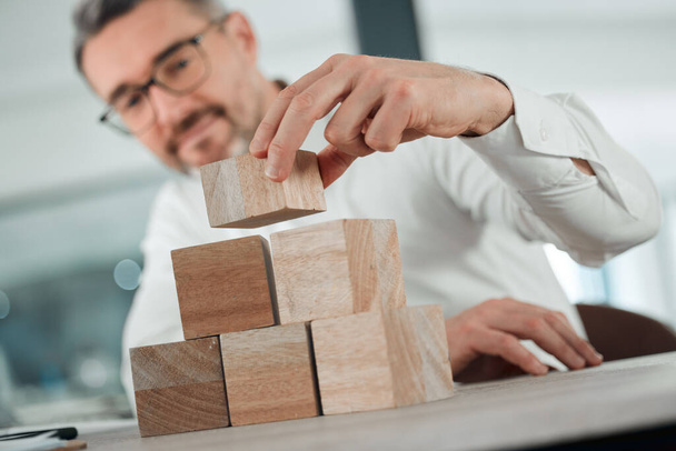 Start building your future from now. Shot of an unrecognisable businessman sitting alone in his office and using building blocks to plan. - 写真・画像