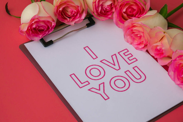 I LOVE YOU greeting card on paper note. Delicate pink roses on pink background. Minimal trendy composition. Romantic pastel pink rose flowers. Preparation for Valentines day, Mothers day, Womens day - Photo, Image