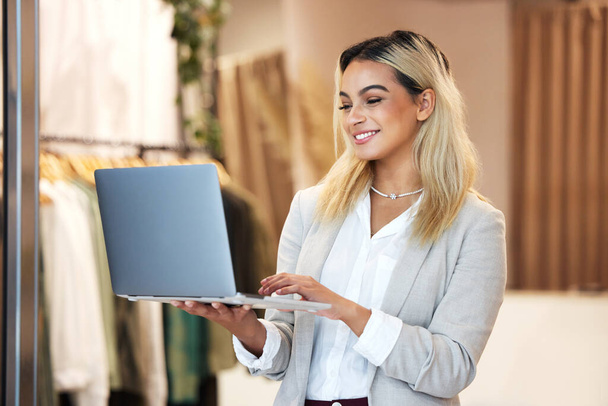 Oben bleiben. Aufnahme einer jungen Geschäftsinhaberin mit einem Laptop in ihrem Bekleidungsgeschäft. - Foto, Bild