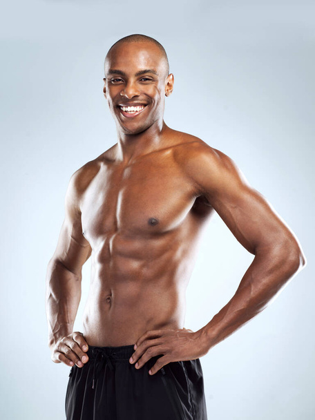 He is built to do this. Studio shot of an cheerful athletic young man posing against a grey background. - Foto, imagen