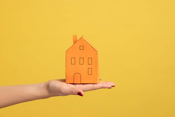 Real estate insurance, repairing services. Closeup of woman hand holding small orange paper house, concept of dream home purchase, mortgage. Indoor studio shot isolated on yellow background. - Fotografie, Obrázek
