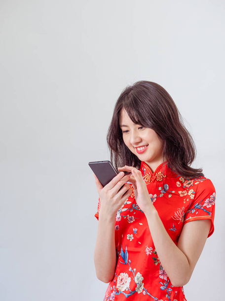 Portrait of a young asian woman wearing traditional cheongsam qipao dress using smartphone on white background. - Фото, зображення