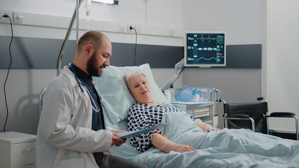 Γιατρός και νοσοκόμα κάνουν συμβουλευτική για άρρωστο ασθενή στο κρεβάτι - Φωτογραφία, εικόνα