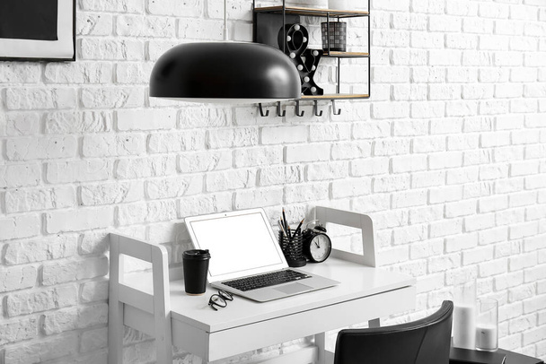 Workplace with modern laptop and paper cup of coffee near white brick wall - Fotografie, Obrázek