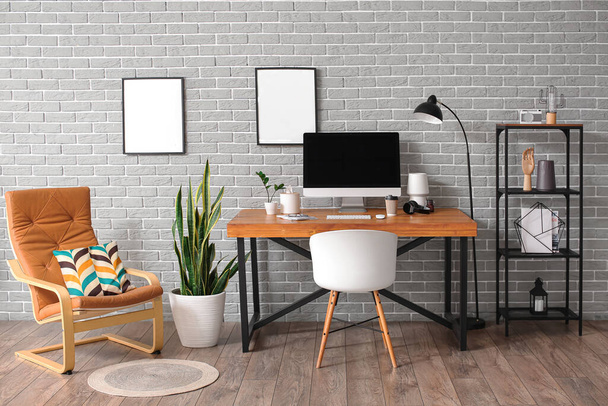 Interior of stylish room with modern workplace and blank photo frames on grey brick wall - Foto, immagini
