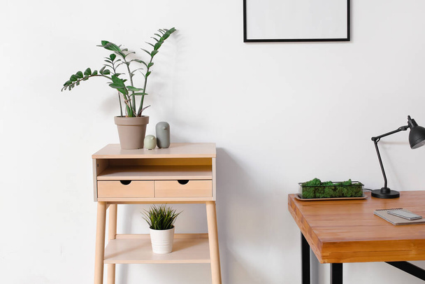 Standing desk with houseplants and wooden table with mobile phone and notebook near light wall - Foto, Imagem