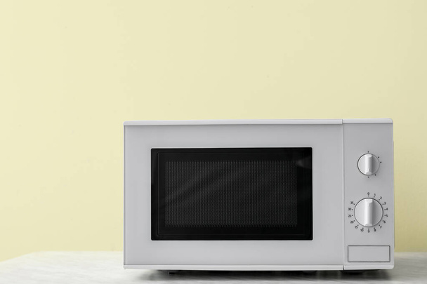 Microwave oven on table against color background - Фото, изображение