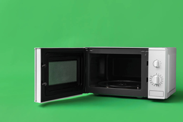 Белая микроволновая печь с открытой дверью на зеленом фоне - Фото, изображение