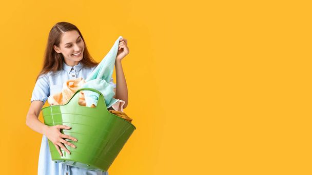 Beautiful woman with laundry in green basket on yellow background - Photo, image