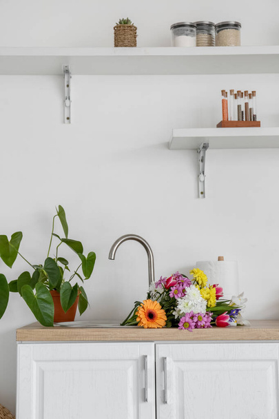 Modern light kitchen with bouquet of flowers in sink - Foto, afbeelding