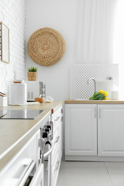 Кухонні лічильники з посудом і тюльпанами в раковині біля білої стіни
 - Фото, зображення