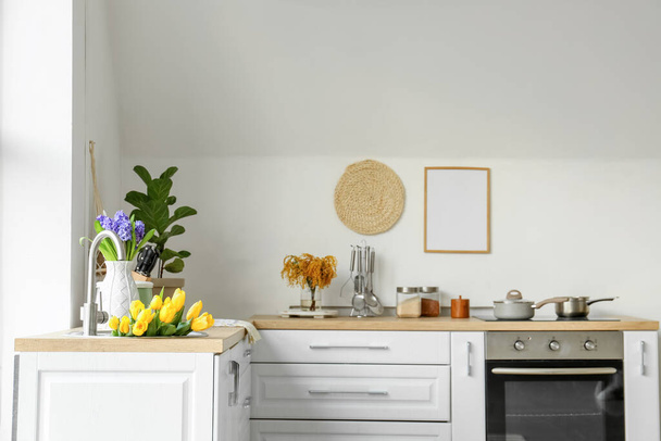 Тюльпани в сучасній раковині і різний посуд на кухонних прилавках біля білої стіни
 - Фото, зображення