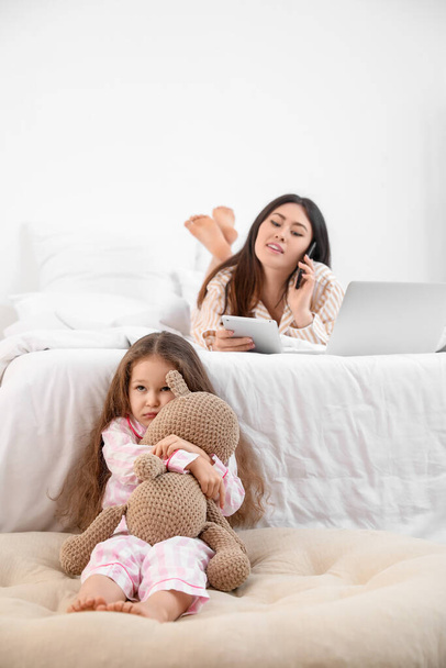 Sad little daughter with working mother in bedroom - Photo, Image