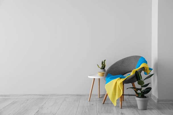 Grey armchair with flag of Ukraine, table and houseplants near light wall - Фото, зображення