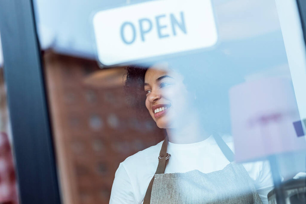 Portrait of beautiful young woman hanging the open sign on a glass door in the pastry shop. - Foto, Imagen