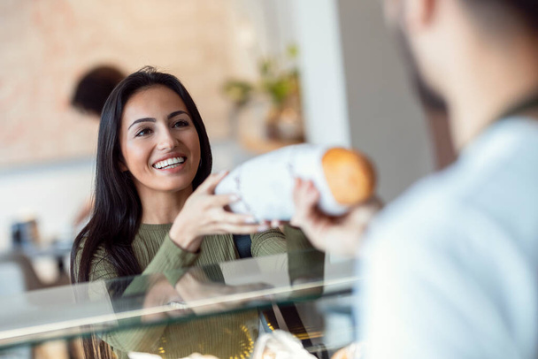 Colpo di venditore allegro dare pane fresco alla donna sorridente in pasticceria. - Foto, immagini