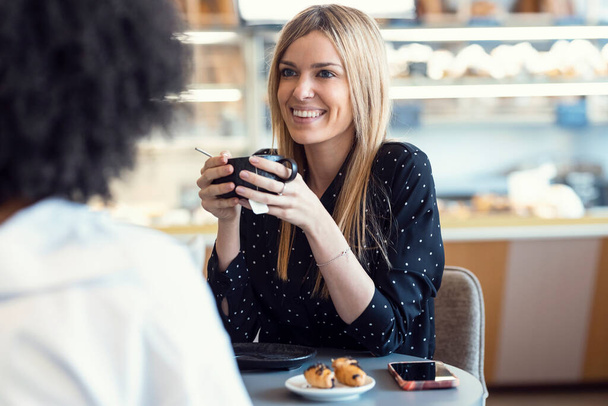 Shot of young happy women talking and laughing while drinking coffee together in pastry shop. - Photo, Image