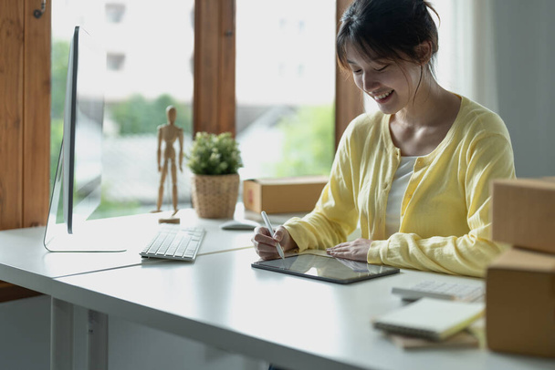 Jovem designer criativo asiático segurando caneta estilete desenho na tela do tablet digital enquanto sentado no escritório moderno. - Foto, Imagem