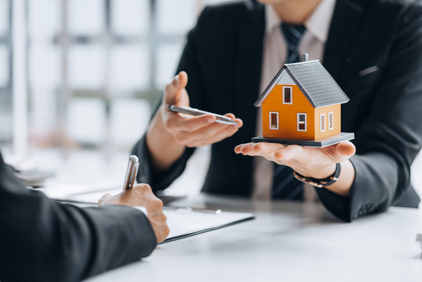 A real estate salesman holding a model of a small house to introduce customers, a sample house project where a salesperson advises customers. The concept of selling houses in the project. - Photo, image