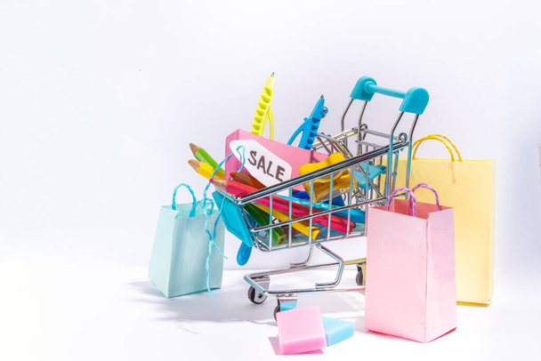School sale concept. Shopping supermarket cart with colorful paper bags, school education supplies and accessories. Back to school shopping background, copy space - 写真・画像