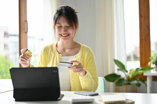 Attractive and happy asian young woman enjoys online shopping at home and pays with credit card. - Photo, Image