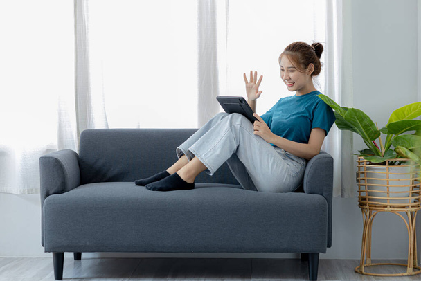 mujer jugando tableta en el sofá en su casa sala de estar, ella está descansando los fines de semana después de un duro trabajo, se relaja viendo películas, escuchando música y videollamadas con la familia en la tableta. - Foto, Imagen
