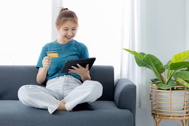 A woman playing smartphone on the sofa in her home living room, she is relaxing on weekends after a hard day's work, she is shopping online and paying by credit card. Credit card payment concept. - Foto, Imagen