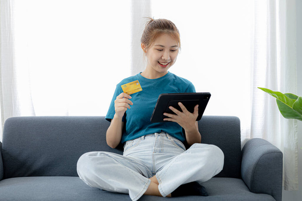 A woman playing smartphone on the sofa in her home living room, she is relaxing on weekends after a hard day's work, she is shopping online and paying by credit card. Credit card payment concept. - Photo, image