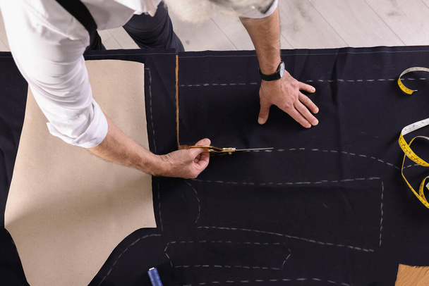 Professional tailor cutting fabric by following chalked sewing pattern at table, top view - Fotoğraf, Görsel