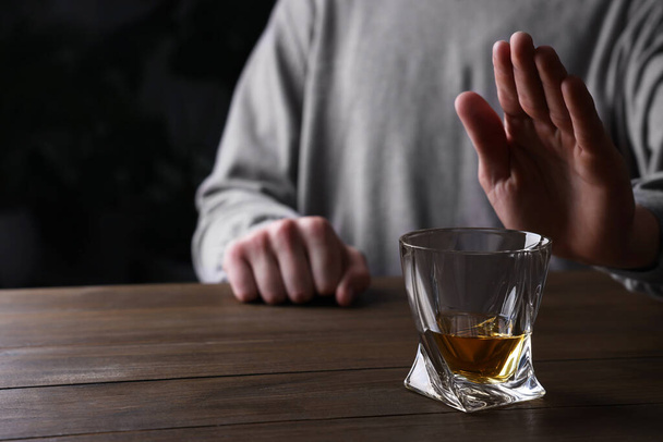 Man refusing to drink whiskey at wooden table, closeup. Alcohol addiction - Fotó, kép