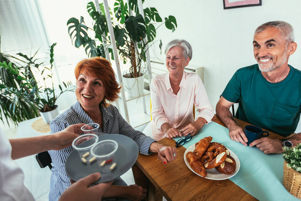 A nővér gyógyszert ad az idősek csoportjának az idősek otthonában..  - Fotó, kép