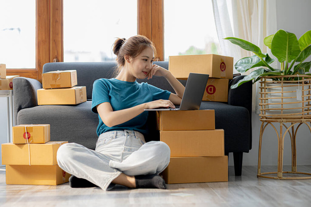 Owner of the online store on the website is preparing the parcels to send to the customers according to the orders from the web page, she is checking the information and preparing to deliver the goods - Φωτογραφία, εικόνα