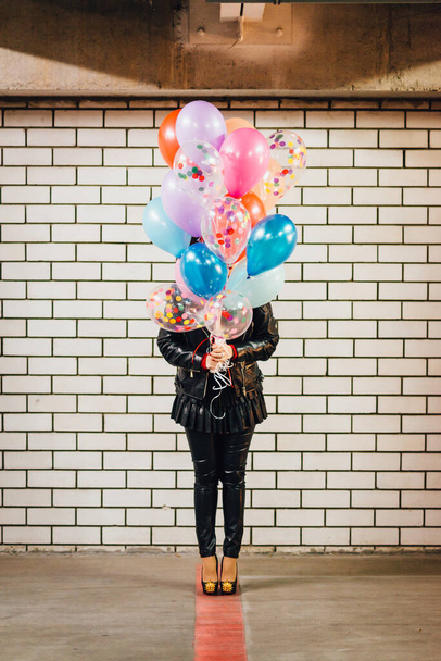 Meisje met de bos van veelkleurige ballonnen staan in de voorkant van de witte bakstenen muur op de parkeerplaats - Foto, afbeelding