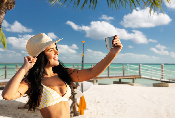 smiling woman in bikini taking selfie on beach - 写真・画像