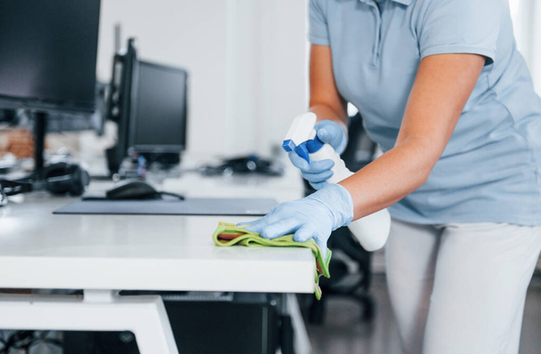 Close up view of woman in protective gloves that cleaning tables in the office. - Photo, Image