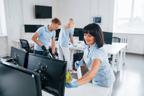 Cleans monitor. Group of workers clean modern office together at daytime. - Foto, imagen