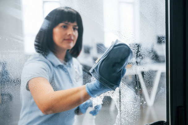 Woman cleaning dirty window by using towel. View through the glass. - Zdjęcie, obraz