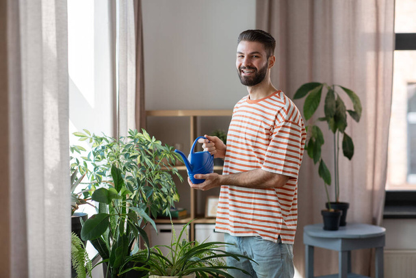 happy smiling man watering flowers at home - Foto, immagini