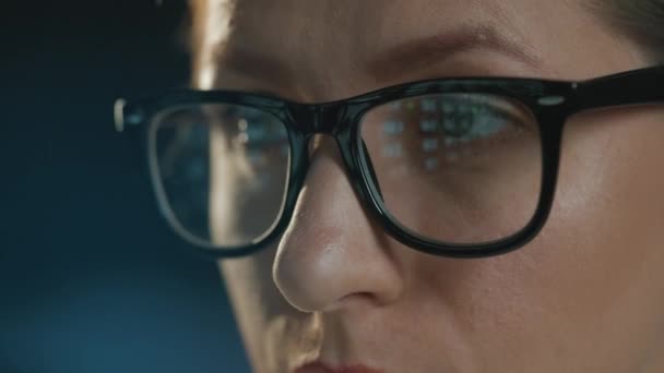 Woman in glasses looking on the monitor and working with data and analytics. The monitor screen is reflected in the glasses. Work at night. Extreme close-up - Imágenes, Vídeo
