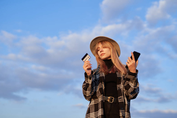 Girl in hat holding smartphone and credit card online shopping - 写真・画像